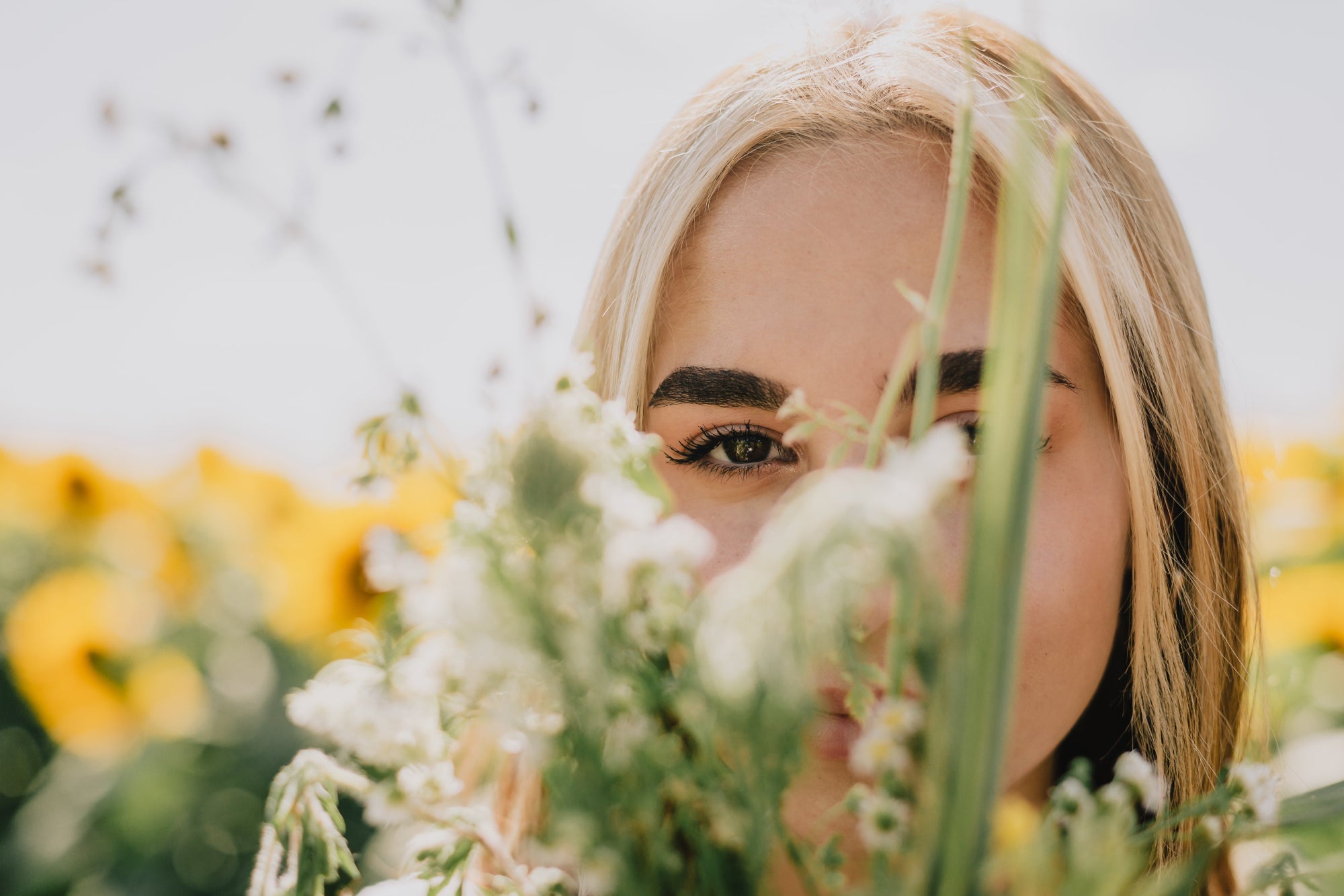 Woman with healthy hair behind wildflowers — natural hair growth products UK, scalp elixir, buy anti-frizz products and hair volume products online.